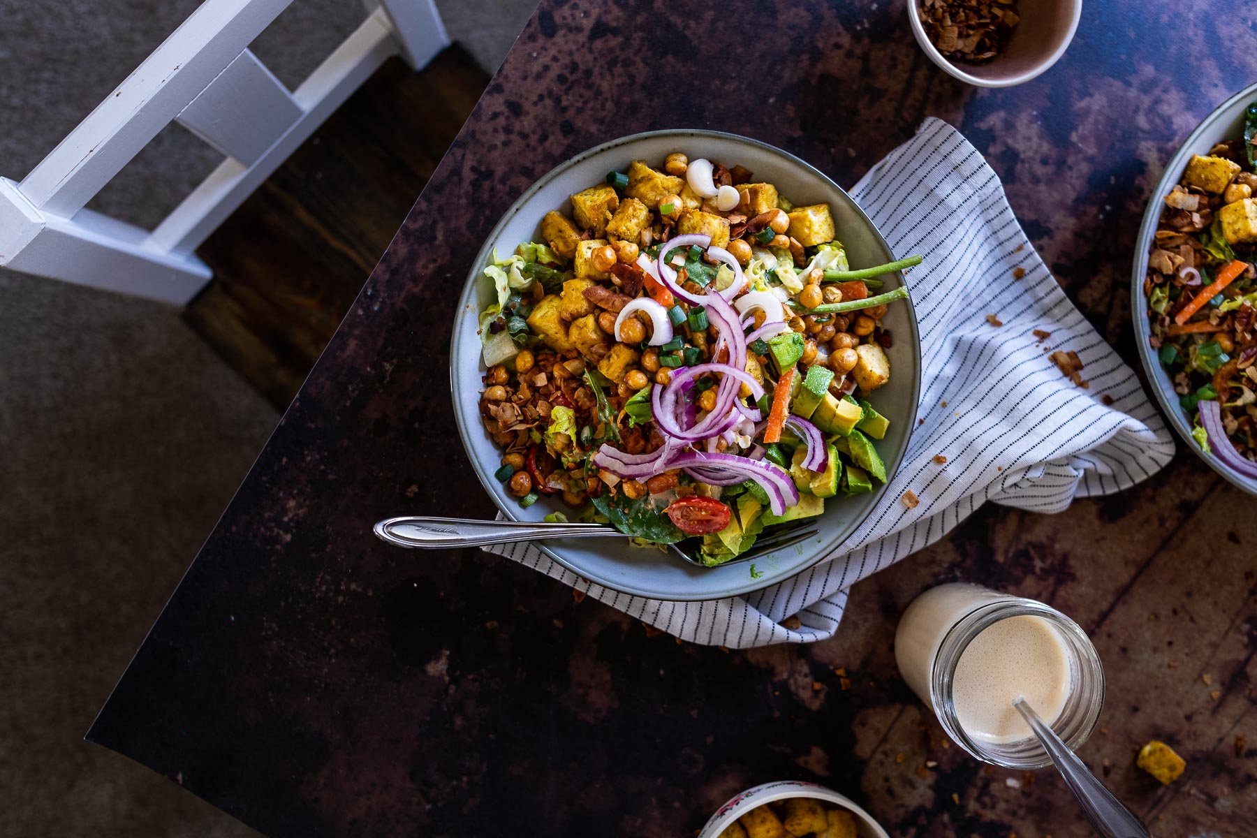 A bowl filled with vegan cobb salad on a table with a chair in the background