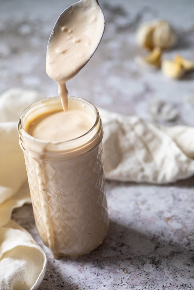 spoon with garlic sauce over a jar with vegan garlic yogurt sauce