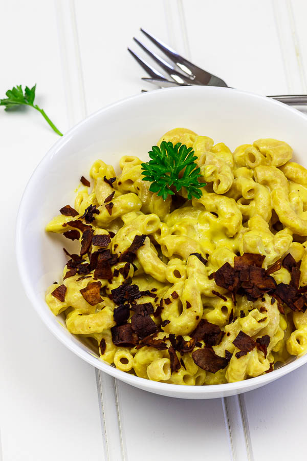 A white bowl of creamy vegan mac and cheese with coconut bacon