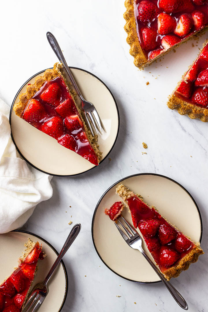 3 plates with vegan strawberry jello cake slices and the whole cake in the upper right corner