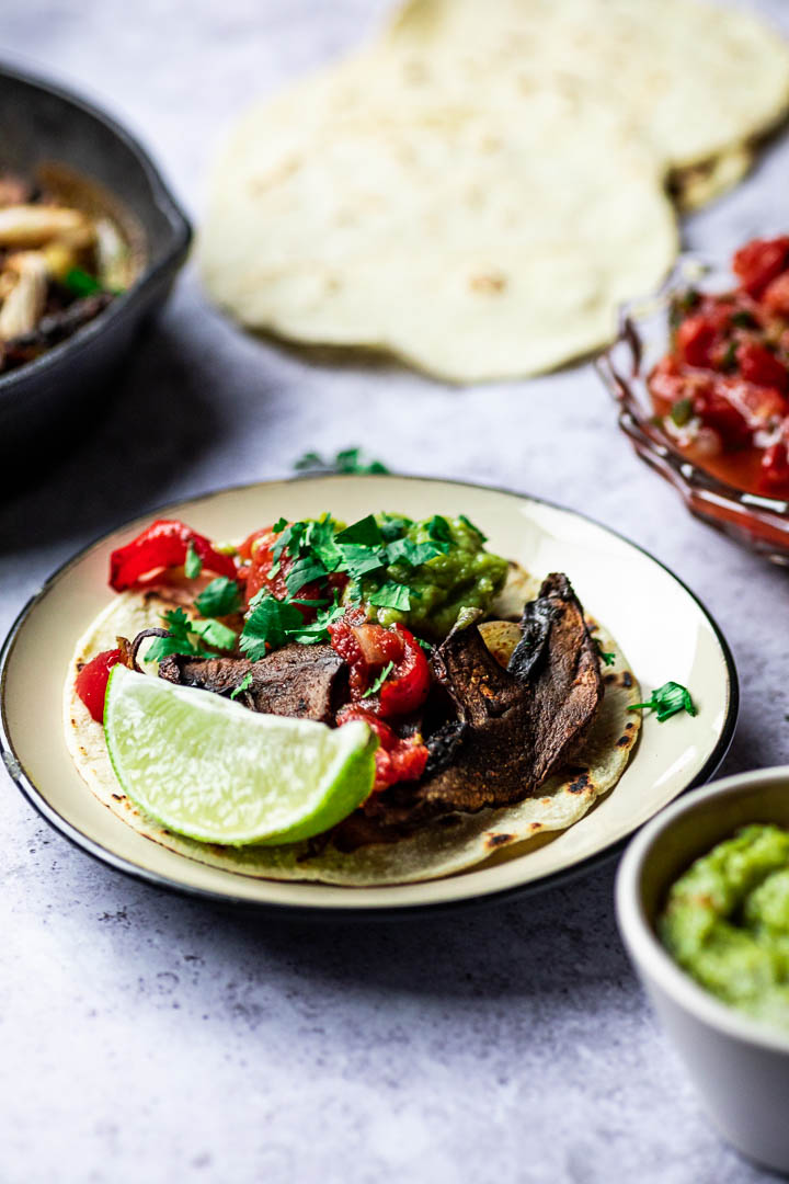 Vegane Blech Fajitas mit Portobello Pilze, Paprika, Zwiebeln serviert in einer gusseisernen Pfanne mit Tortillas, Salsa und Guacamole