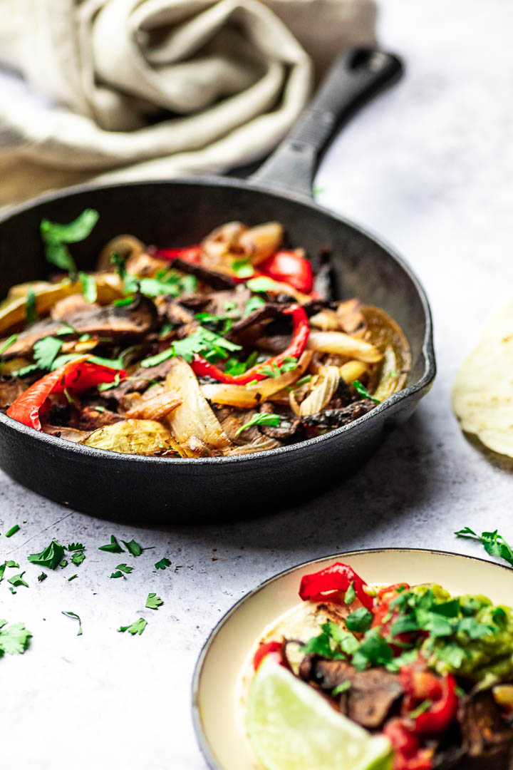 Vegan Sheet Pan Fajitas with Portobello Mushrooms, Bell Peppers, Onions served in a skillet pan with tortillas, salsa and guacamole