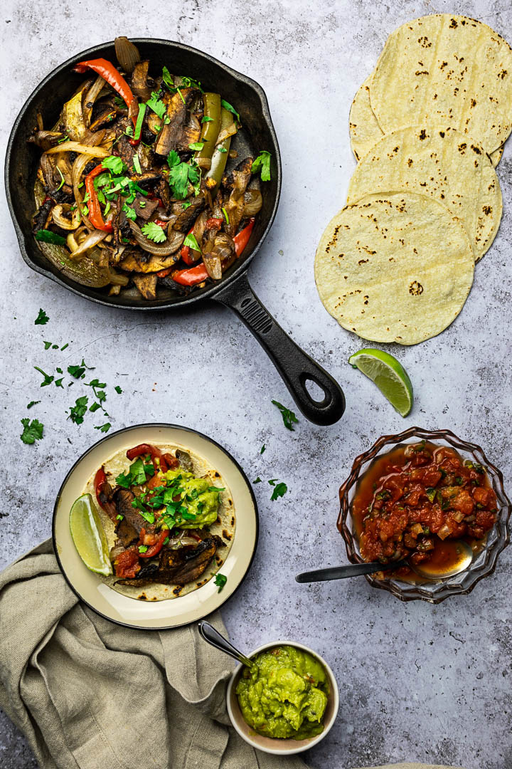 Vegane Blech Fajitas mit Portobello Pilze, Paprika, Zwiebeln serviert in einer gusseisernen Pfanne mit Tortillas, Salsa und Guacamole