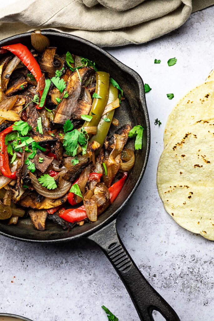 Vegan Sheet Pan Fajitas with Portobello Mushrooms, Bell Peppers, Onions served in a skillet pan with tortillas, salsa and guacamole
