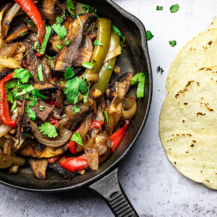 Vegan Sheet Pan Fajitas with Portobello Mushrooms, Bell Peppers, Onions served in a skillet pan with tortillas, salsa and guacamole