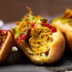 Vegane Wurst zubereitet aus Seitan (Gluten), Kichererbsen, Tahini und Rote Bete. Vegetarische Würstchen als Hot Dog serviert mit Senf, Ketchup, Gewürzgurken und Röstzwiebeln