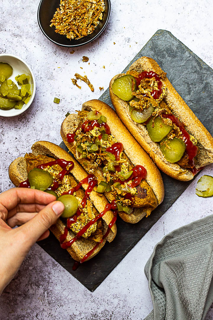 Vegan Hot Dogs made with Seitan (Gluten), Chickpeas, Tahini, Beetroot. Vegetarian Hot Dog with Mustard, Ketchup, Pickles and french fried onions