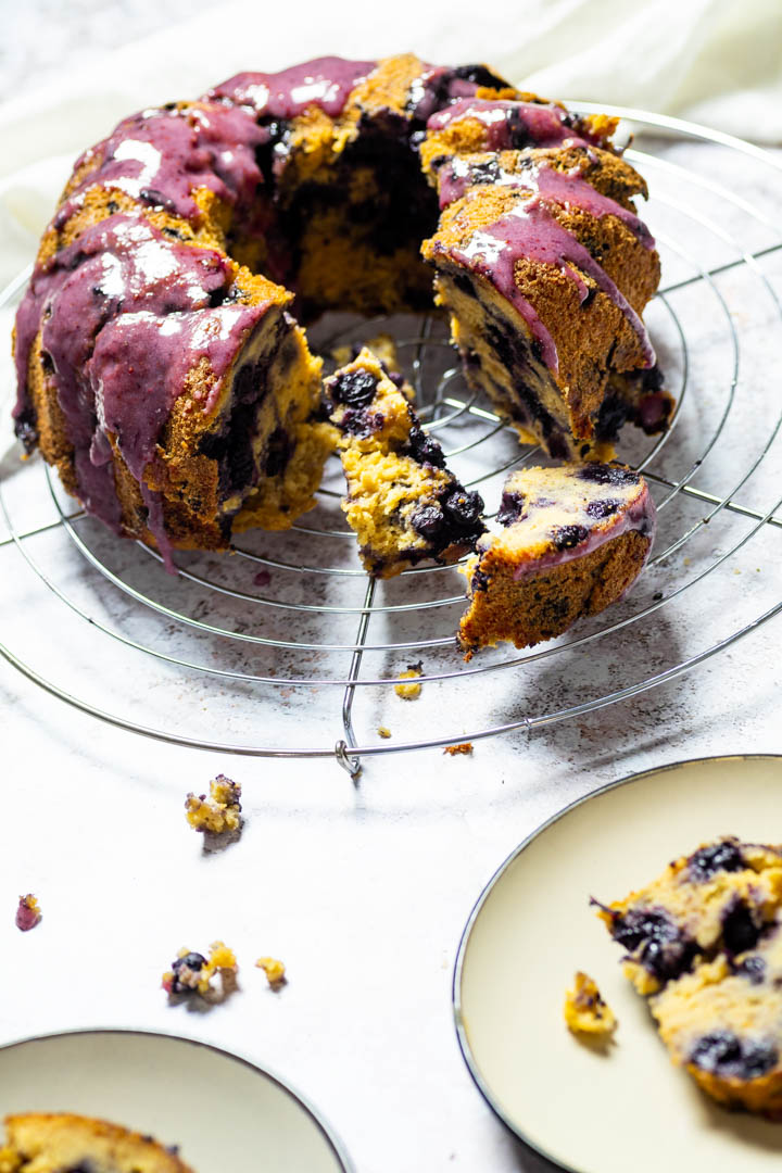 Blueberry Bundt Cake on a wire wrack with focus in the back and in front two slices of blueberry bundt cake on plates.