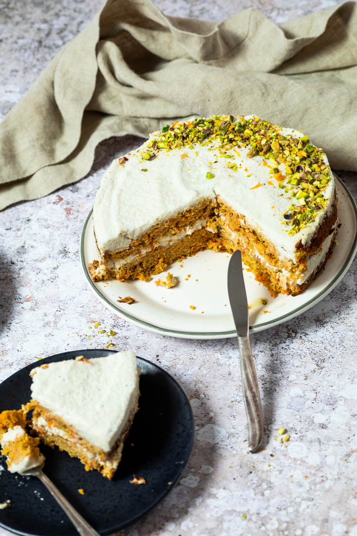 The Whole Carrot Cake on a plate with two missing pieces. You see the layers of the carrot cake.