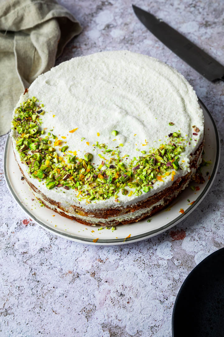 Uncut carrot cake decorated with chopped pistachios and orange zest