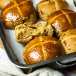 Baking Pan with Hot Cross Buns. One vegan hot cross bun is halfed to see the fluffy and pillowy inside.
