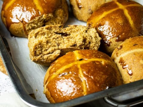 Backform mit Hot Cross Buns. Eins ist halbiert um das fluffige Innere zu sehen.