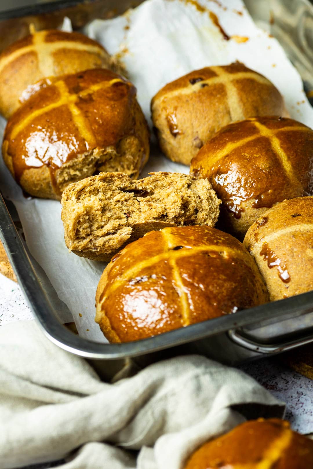 Baking Pan with Hot Cross Buns. One vegan hot cross bun is halfed to see the fluffy and pillowy inside.