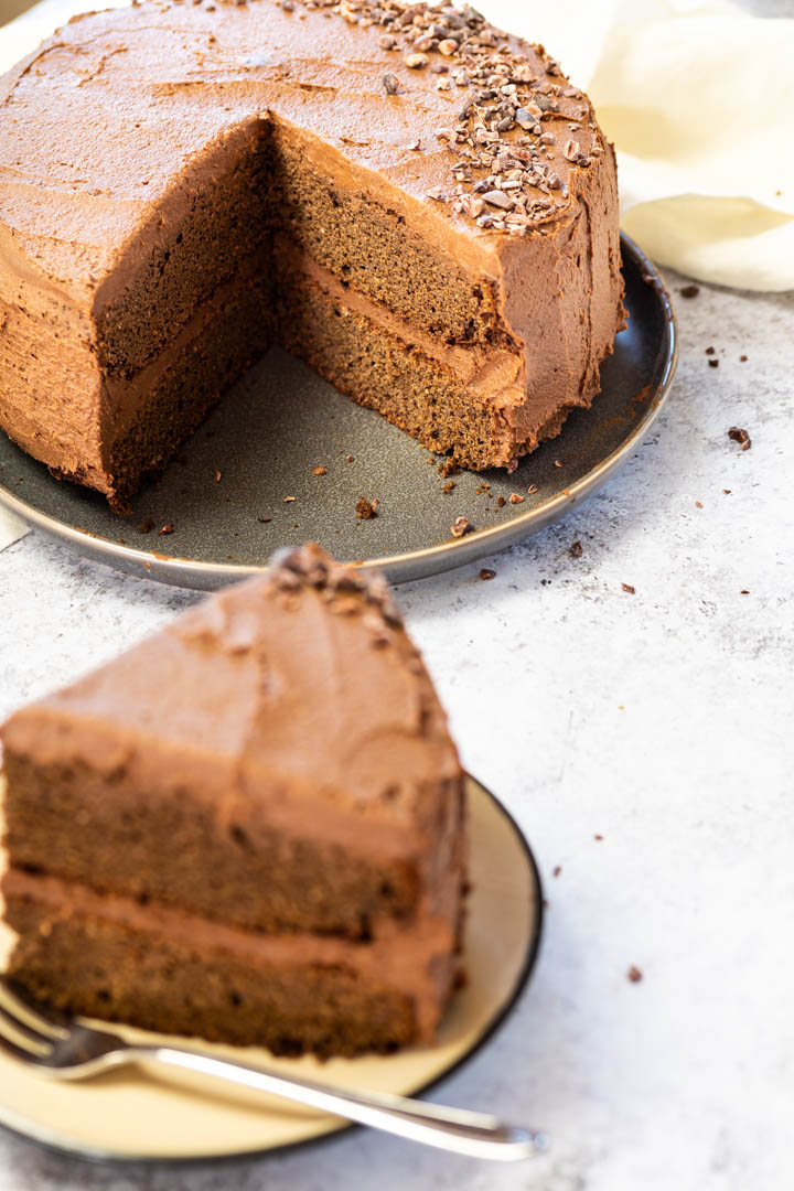 Vegan Chocolate Layer Cake with a missing piece. In the front a blurred cake piece on a plate