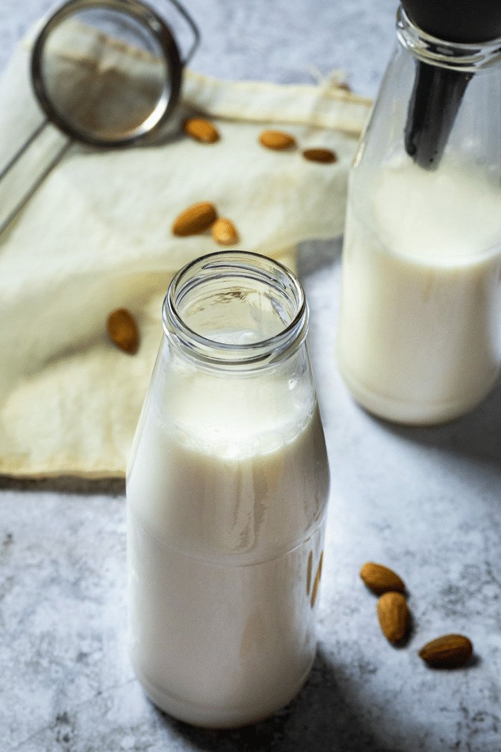 Hausgemachte Mandelmilch in einem Glas und im Hintergrund ein Sieb und ein Glas mit Mandelmilch