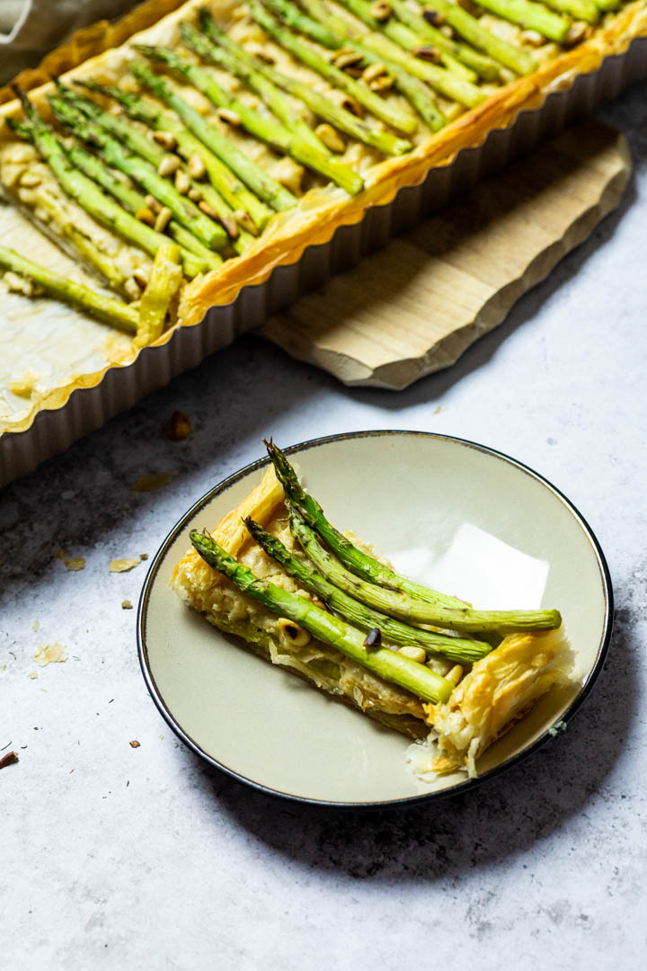 Ein Teller mit einem Stück vegane Spargel Tarte und im Hintergrund die ganze Spargel Tarte.