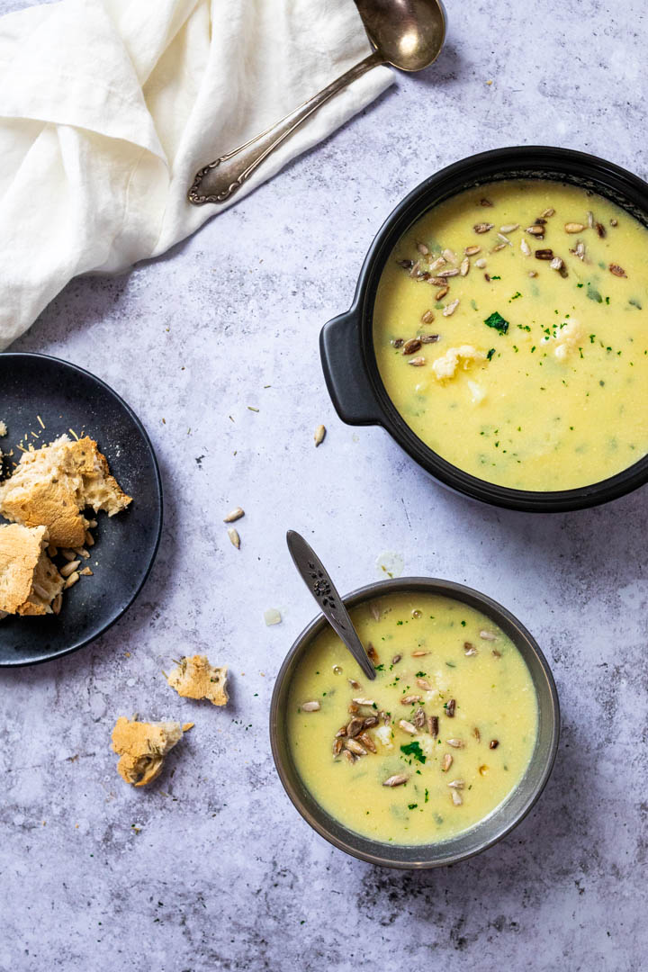 Two bowls with vegan cauliflower soup with some roasted sunflower seeds and parsley.