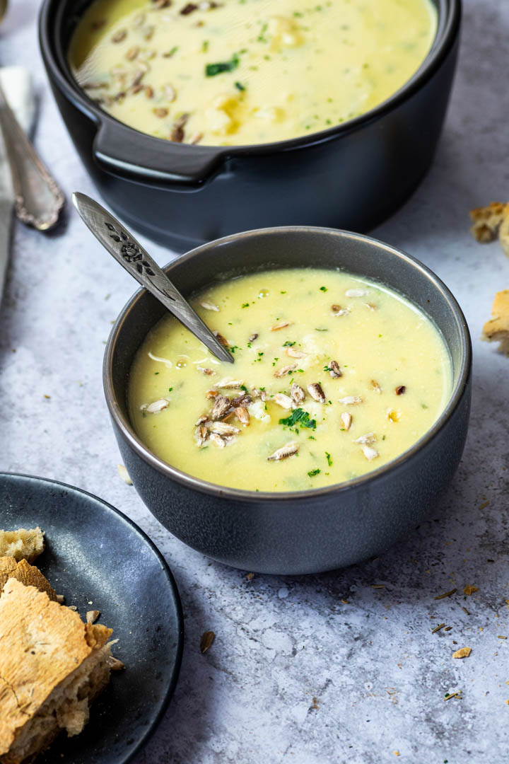 A bowl with vegan cauliflower soup and in the background is a pot with cauliflower soup.