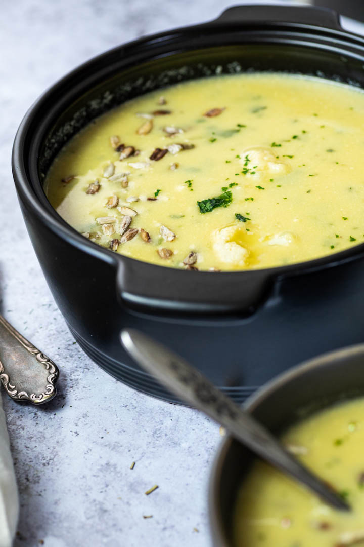 Close up of a pot with cauliflower soup with one bowl blurred in front.