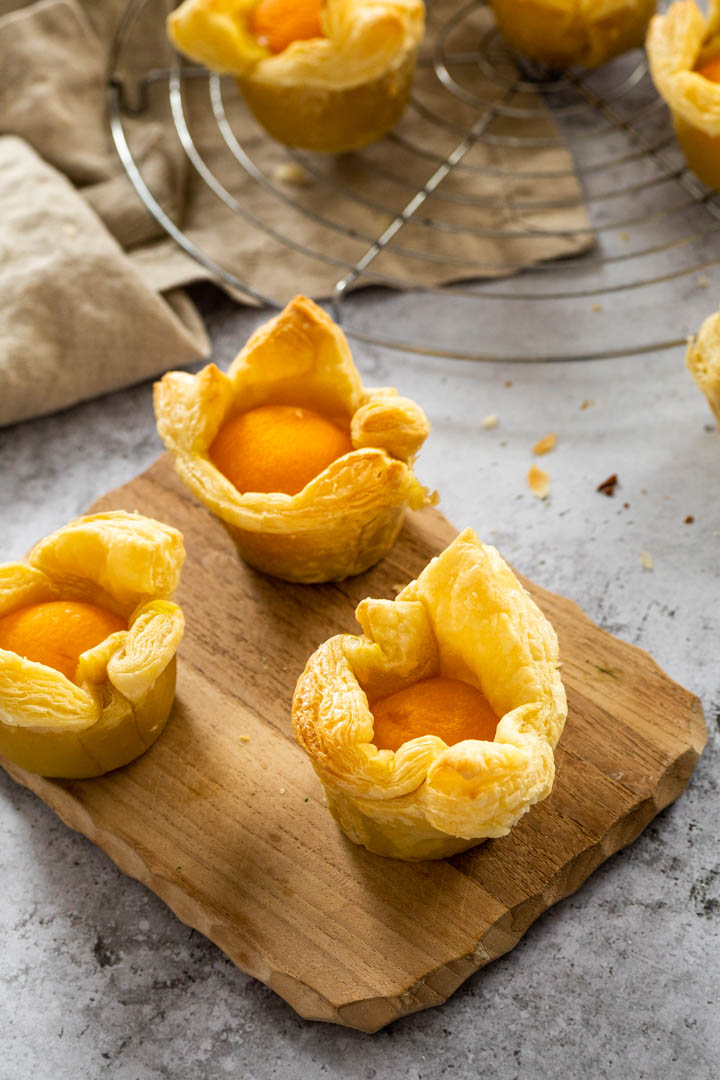 3 vegan custard apricot cups on a wooden board with a blurred wire rack in the background