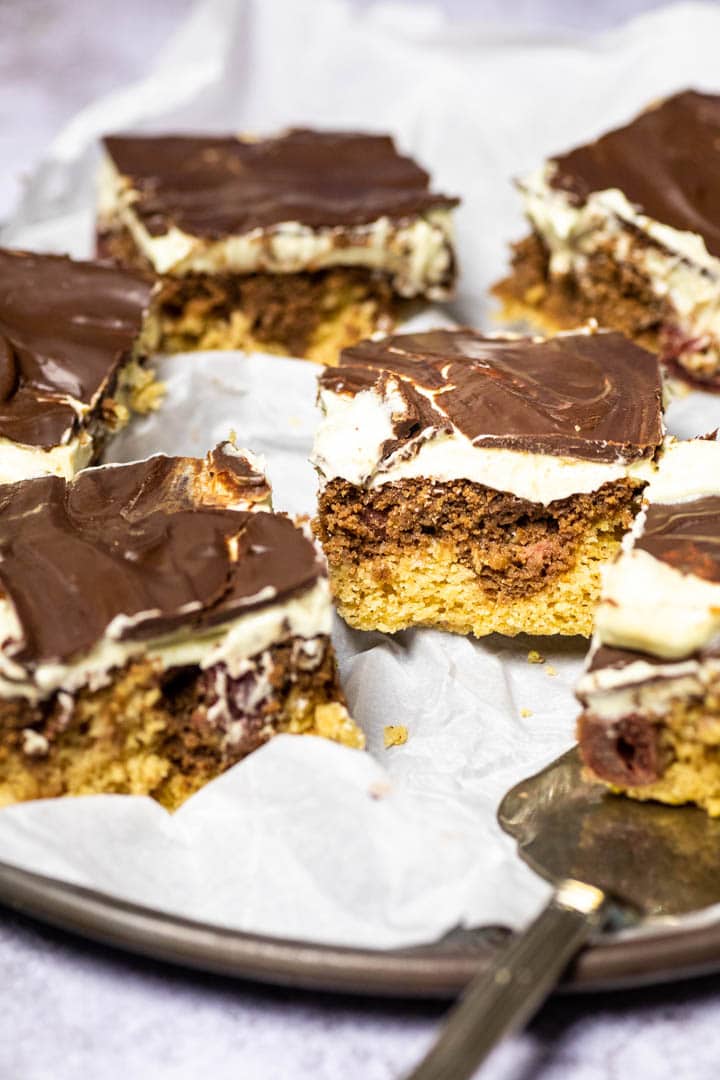 A couple pieces of the vegan custard cherry chocolate cake (Donauwelle) on a plate with some are blurred out to focus the middle cake.