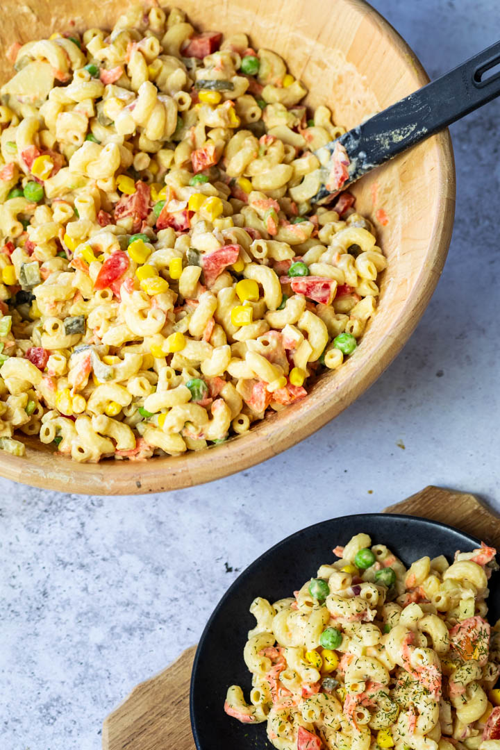 A bowl with vegan macaroni salad and a plate on the left lower part of the photo