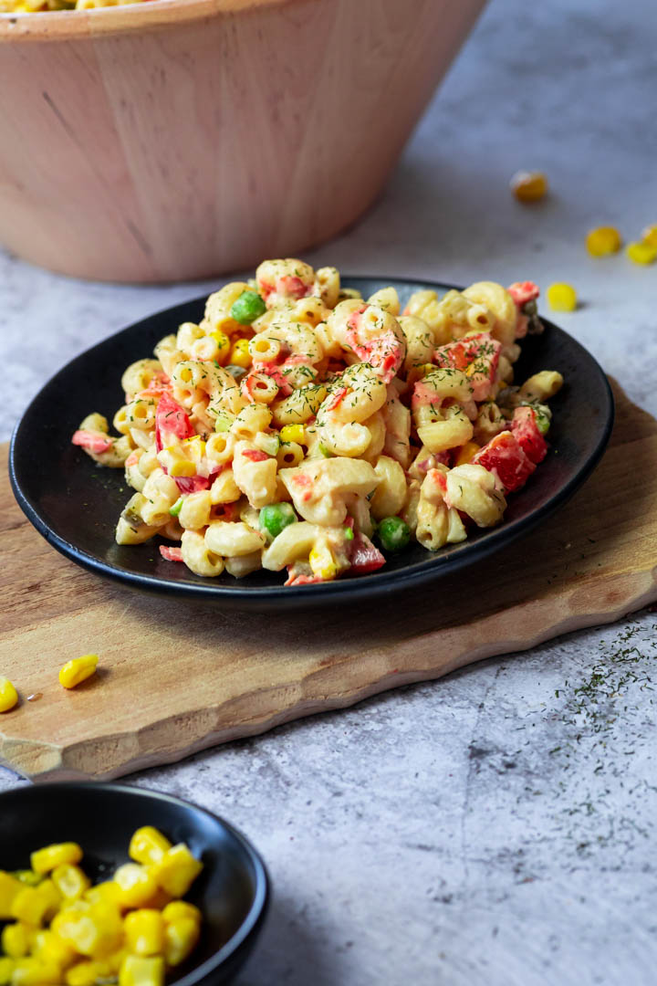 A plate full with vegan macaroni salad on a wooden board.