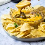 Tortilla Chips in vegane Nacho Käse Sauce gedippt.