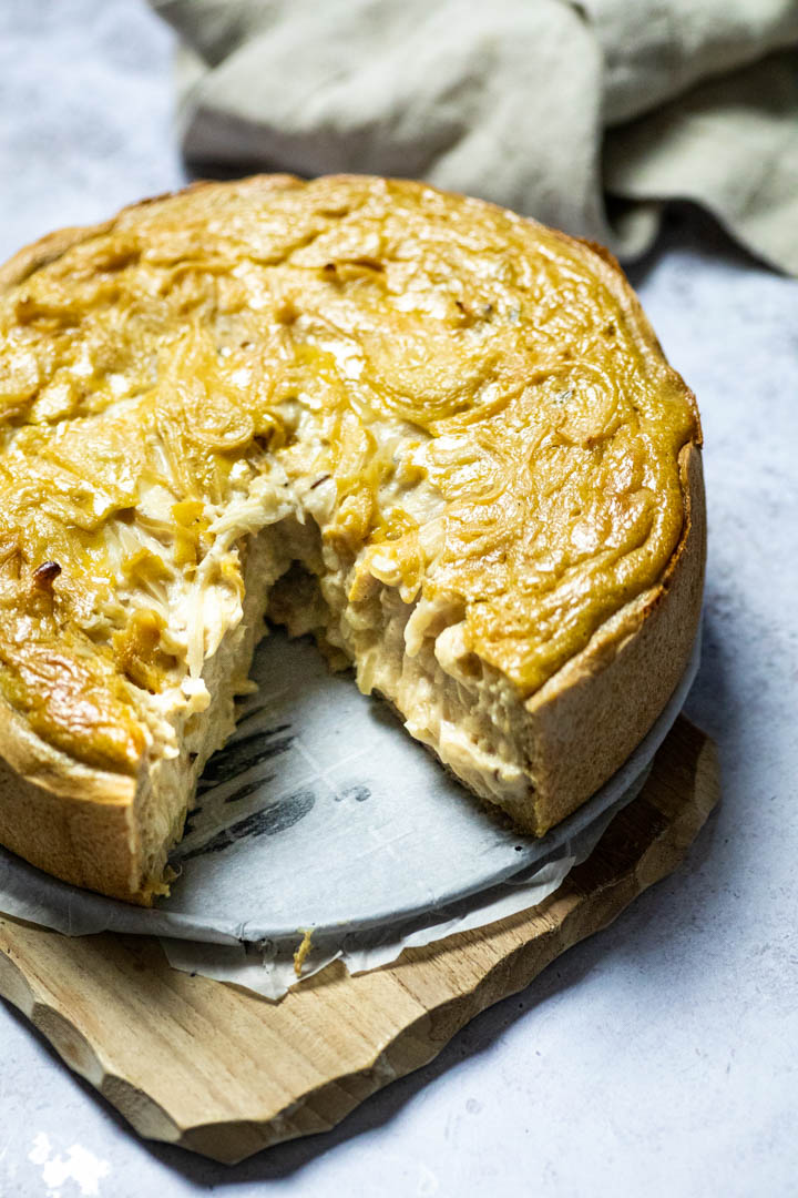 Ganzer veganer Zwiebelkuchen auf einem Holzbrett mit einem fehlenden Stück