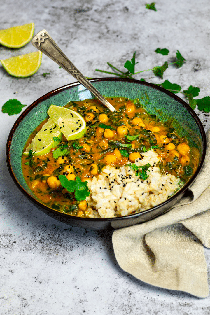 Kichererbsen Curry mit Spinat in einer Schüssel mit Reis serviert und garniert mit Limettenscheiben und Koriander