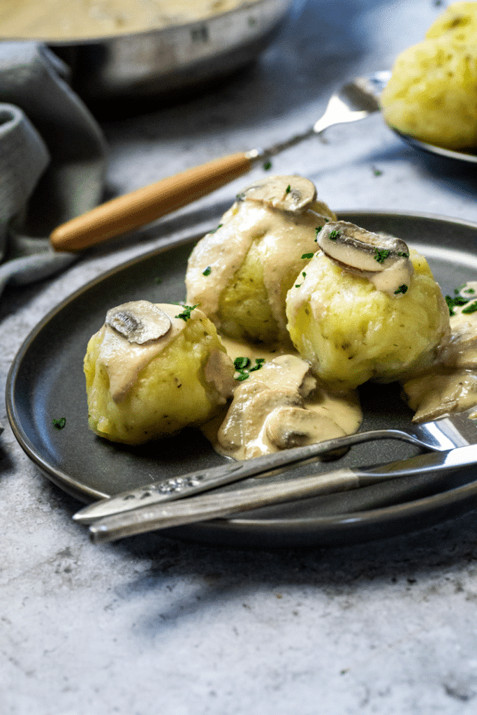 3 vegan potato dumplings on a plate with mushroom sauce