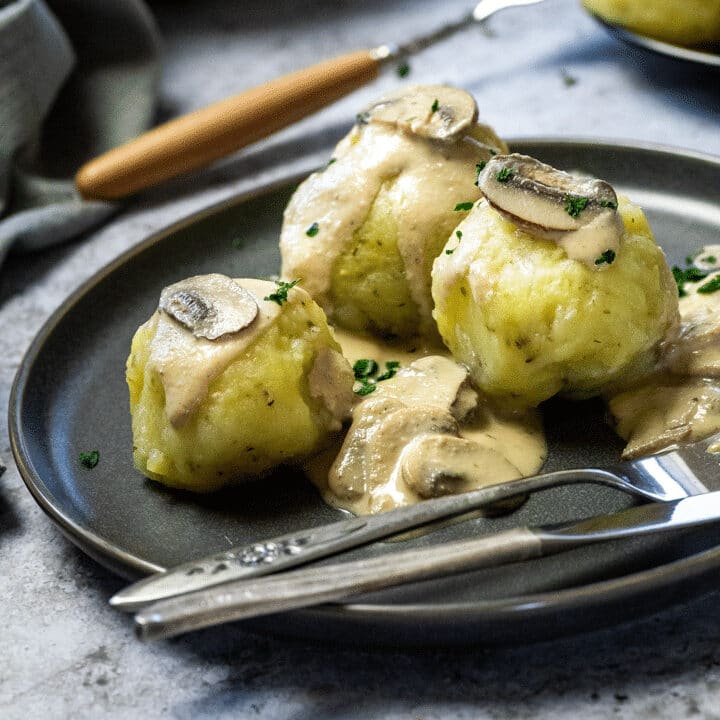 3 vegan potato dumplings on a plate with mushroom sauce