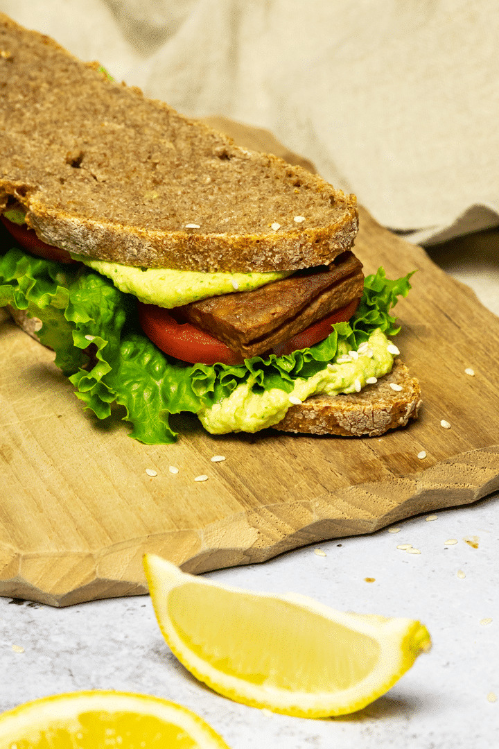 Vegan BLT Sandwich on a board made with tofu bacon, lettuce and tomatoes