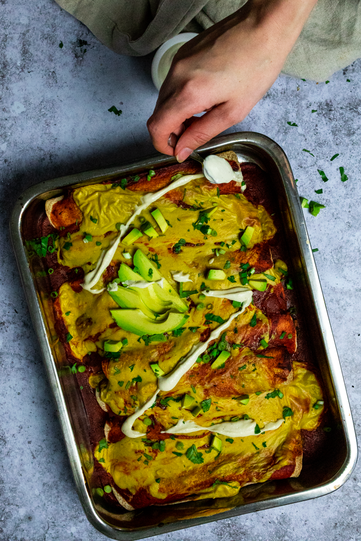 Vogelansicht des Gießens einer veganen sauren Sahne über pflanzliche Enchiladas.