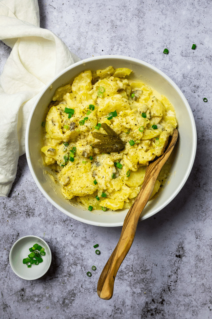 Vogelansicht des veganen cremigen Kartoffelsalats mit einem Servierlöffel