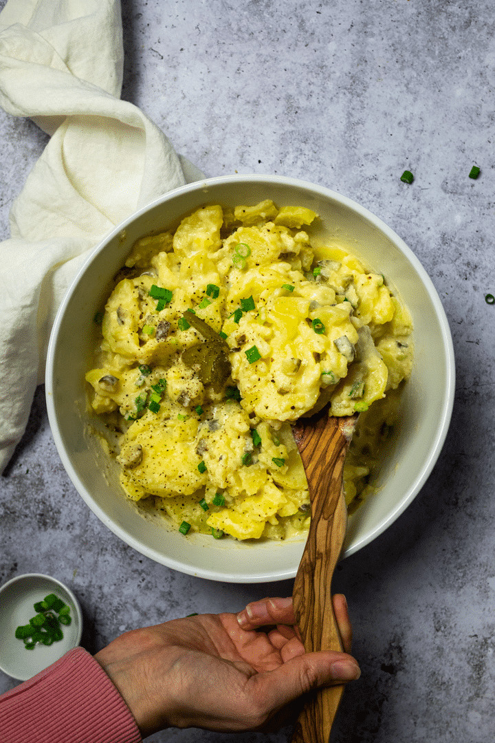 Halte einen Servierlöffel in einer Schüssel mit veganem Kartoffelsalat