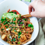 In a bowl some vegan thai peanut noodles and holding some asian sticks