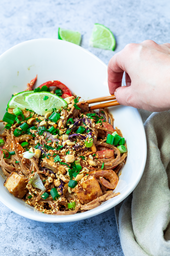 In a bowl some vegan thai peanut noodles and holding some asian sticks