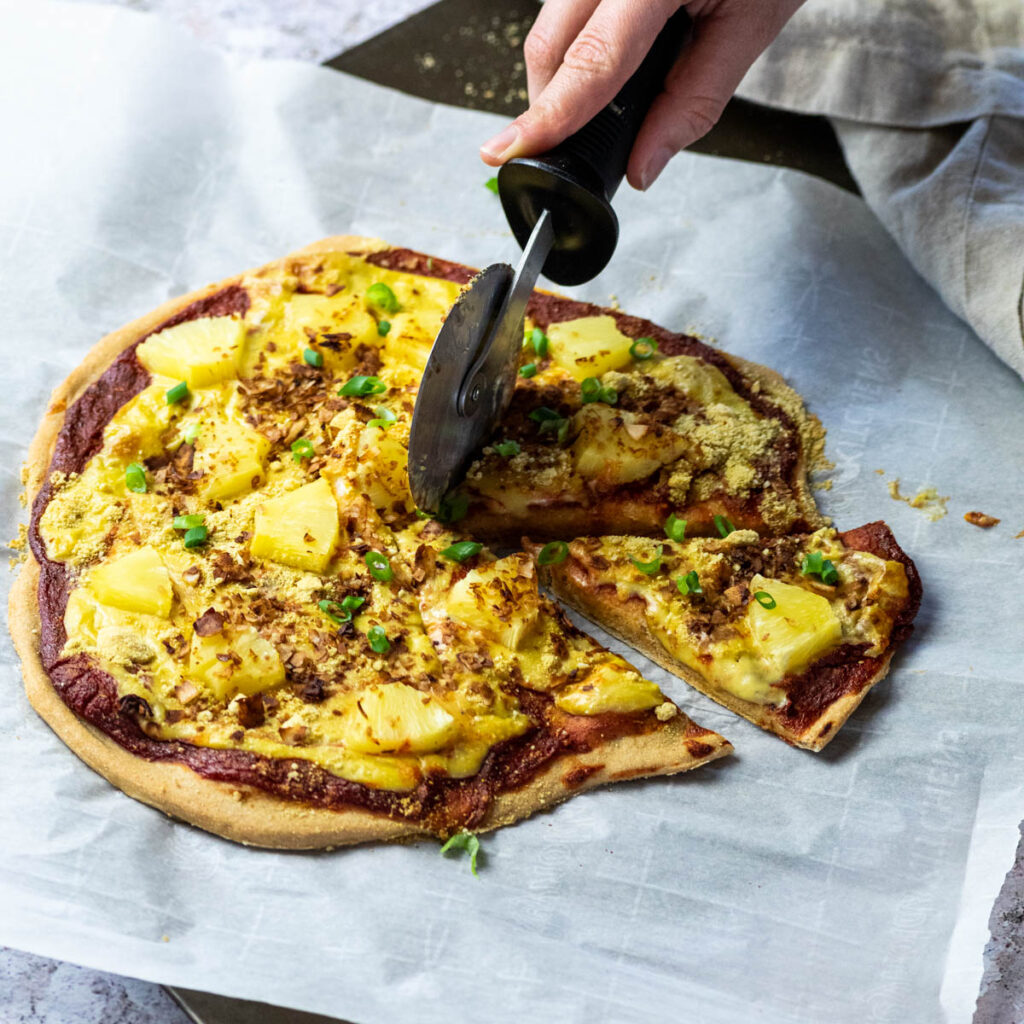 Cutting a vegan pizza hawaii with a pizza cutter