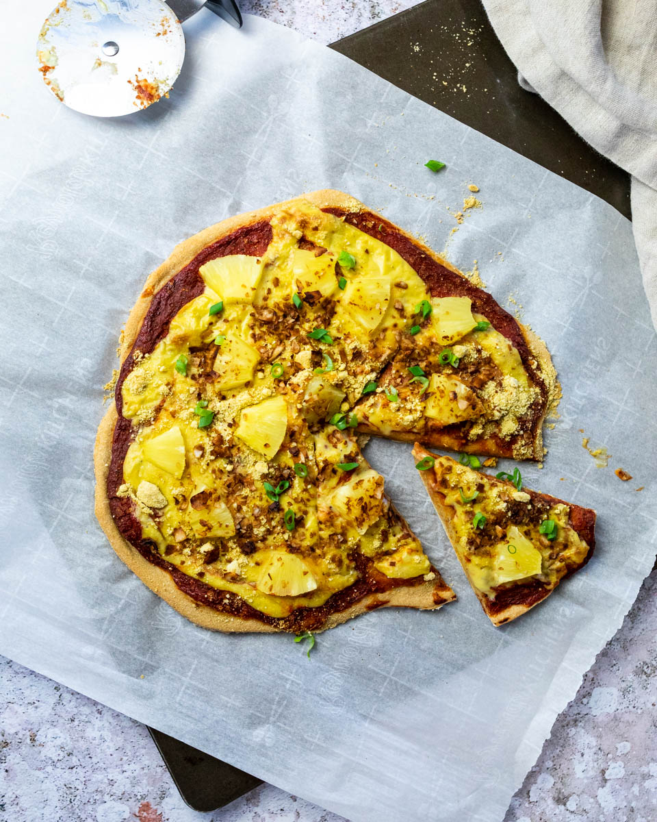 Flatlay der Pizza Hawaii mit einem Stück geschnitten