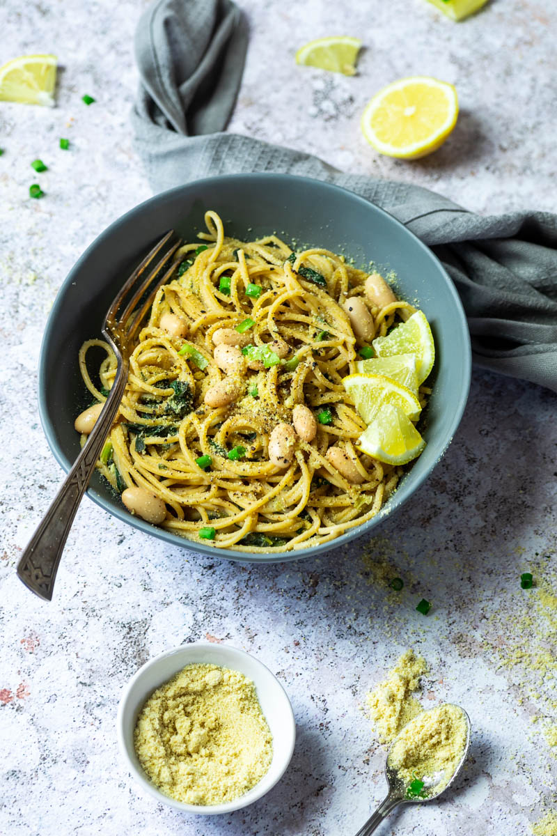 A pasta with a lemon sauce with some vegan parmesan in a small bowl in front of the pasta bowl