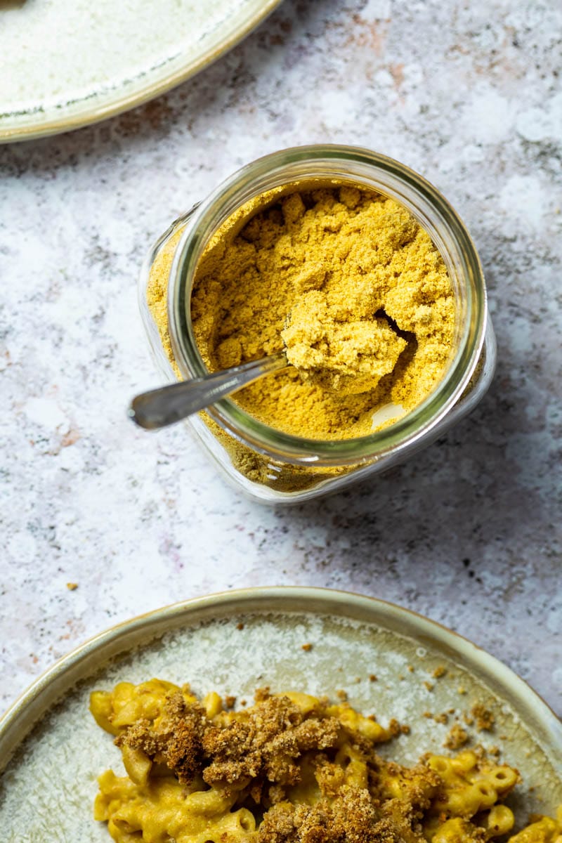 Jar full with homemade vegan mac and cheese powder and a plate with dairy-free mac and cheese in front