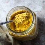 Jar with vegan mac and cheese powder and a spoon with vegan mac & cheese powder over the spoon.