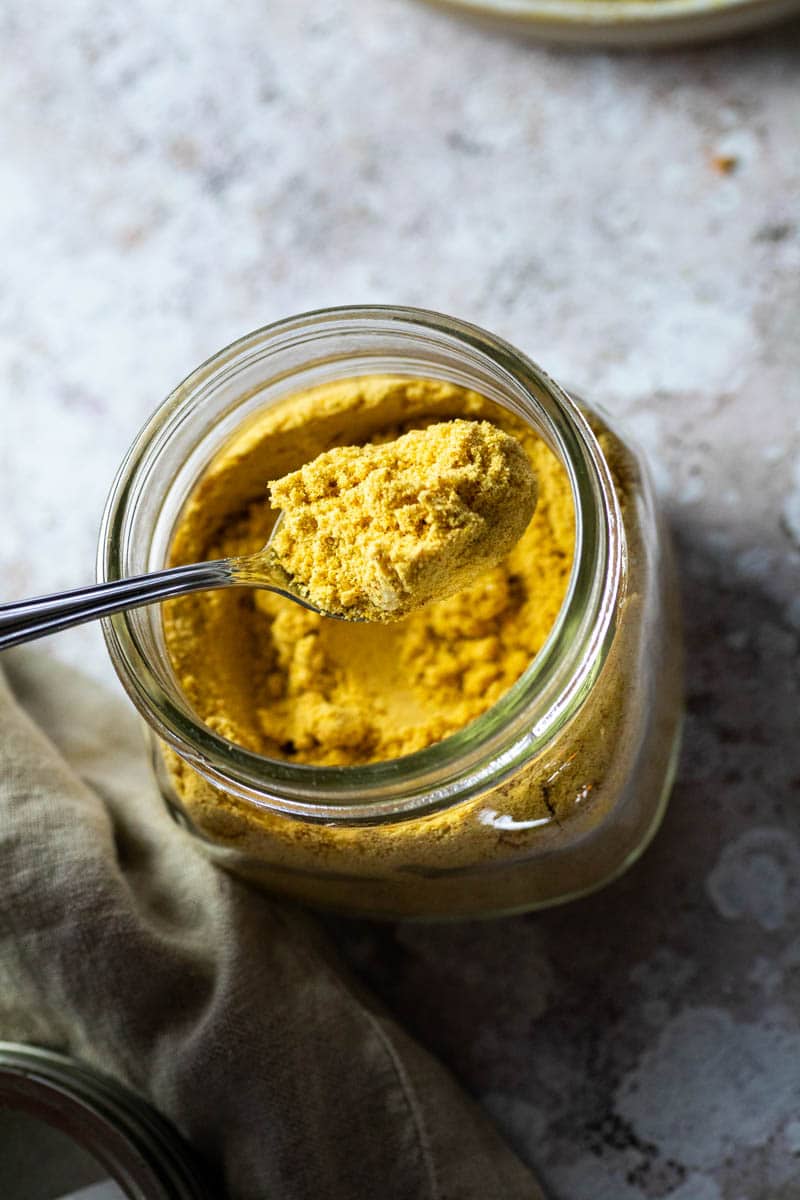 Jar with vegan mac and cheese powder and a spoon with vegan mac & cheese powder over the spoon.