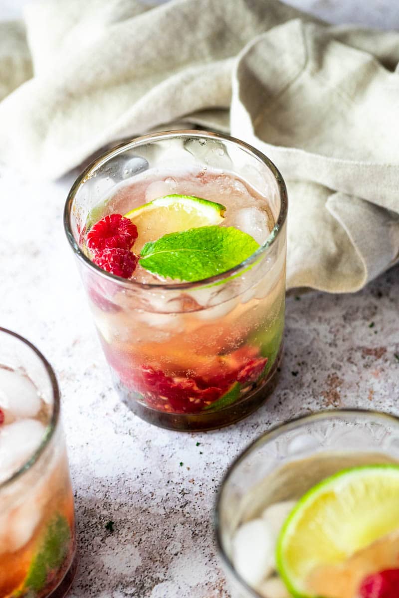 A glass with raspberry mojito and two glasses in front blurred