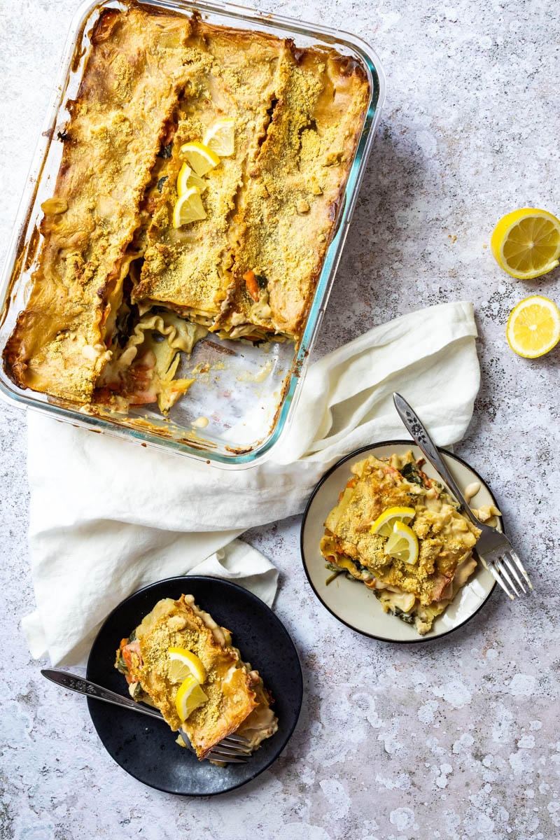 Weiße Lasagne in einer Auflaufform und zwei Teller mit einem Stück veganer weißer Lasagne