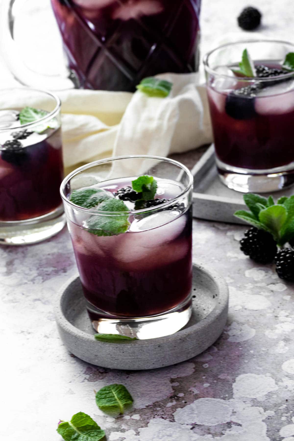 A glass with sugar free blackberry iced tea on a serving plate with glasses and pitcher in the background.