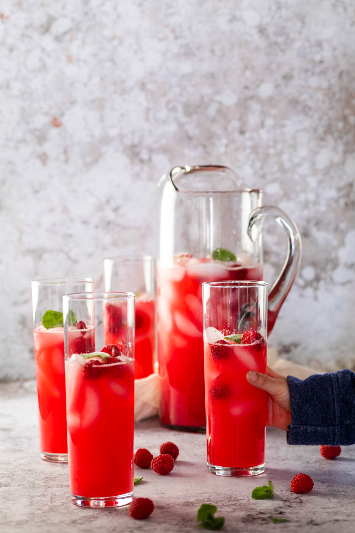 Sugar-free Raspberry Limeade in glasses and pitcher. One glass of raspberry limeade is holding.