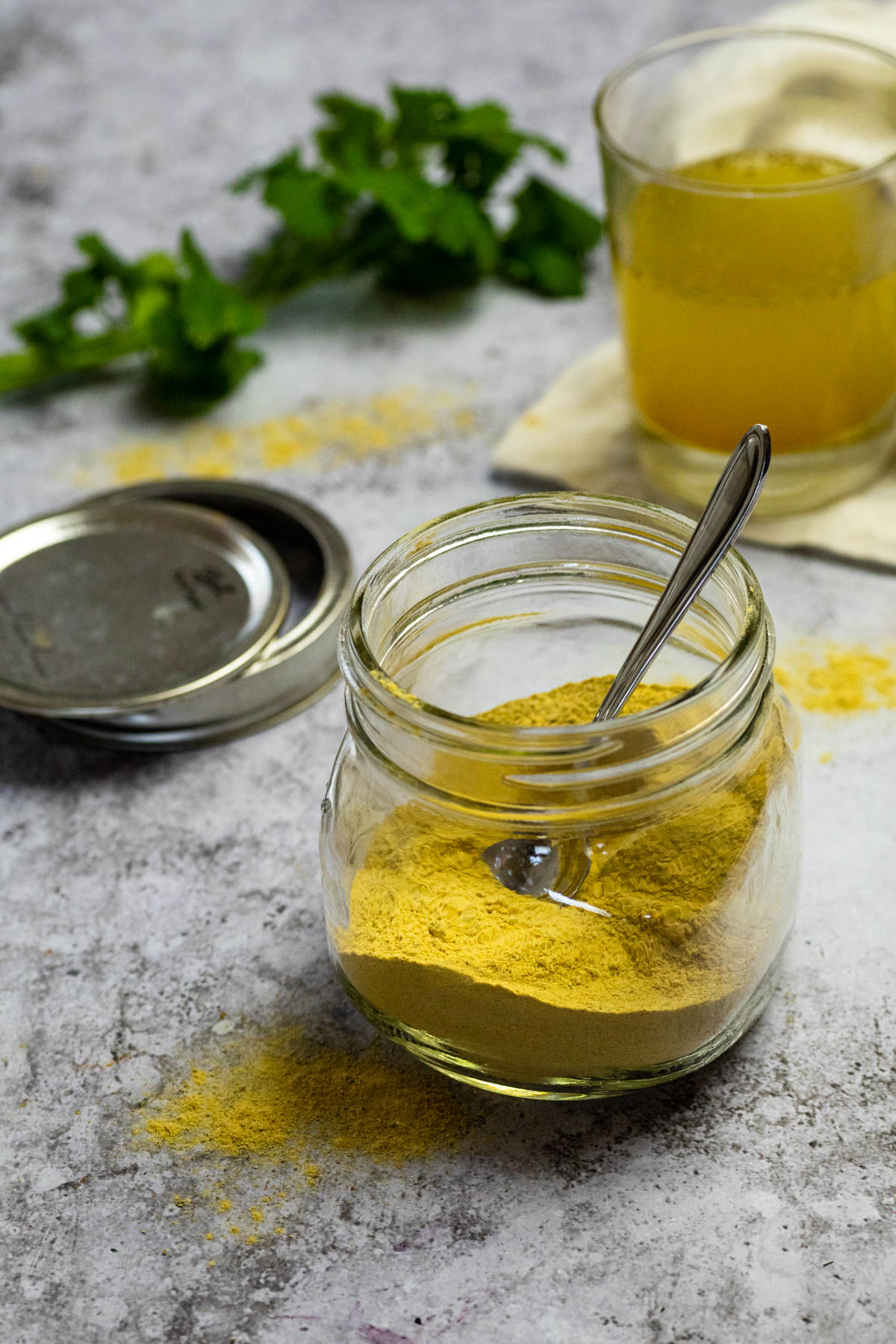 Homemade Vegan Chicken Bouillon Powder in a jar with a spoon. In the background some chicken broth