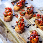 Bruschetta Crostinis serviert auf einem Holzbrett mit einer Crostini im Fokus.